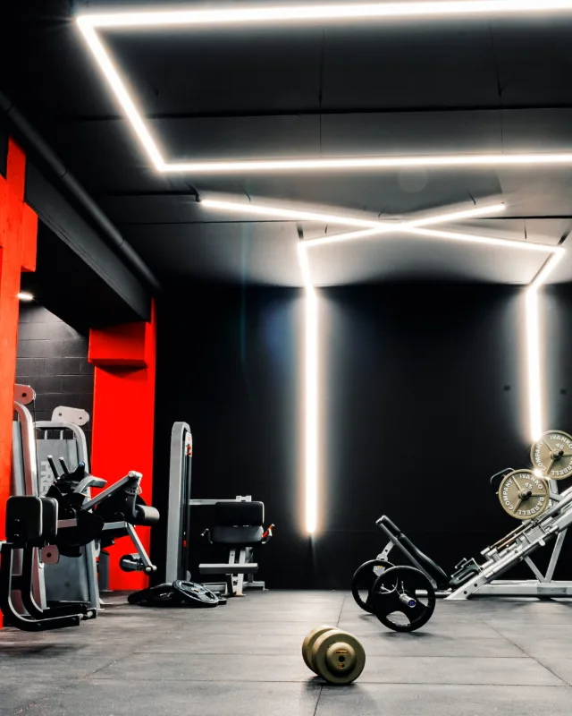 Vista general de la sala de Apex Power Gym, con la pared roja y las tiras de luz